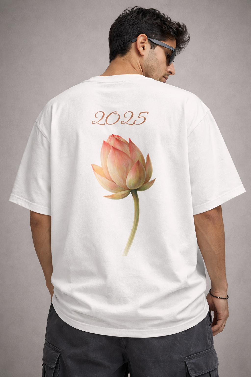 A model from the apparel brand Absolutely Nothing wearing a white oversized t-shirt with a graphic design of a half-bloomed lotus and text that says 2025 on the back while standing against a gray background.