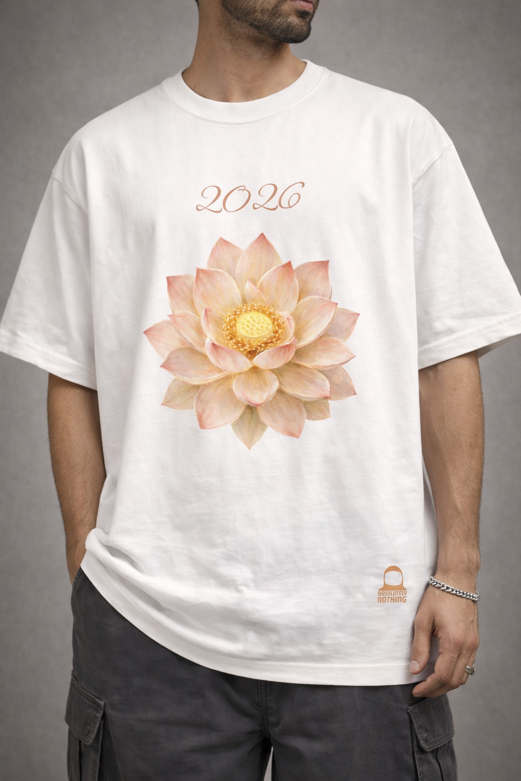 A model from the apparel brand Absolutely Nothing wearing a white oversized t-shirt with a graphic design of a fully-bloomed lotus and text that says 2026 on the front while standing against a gray background.